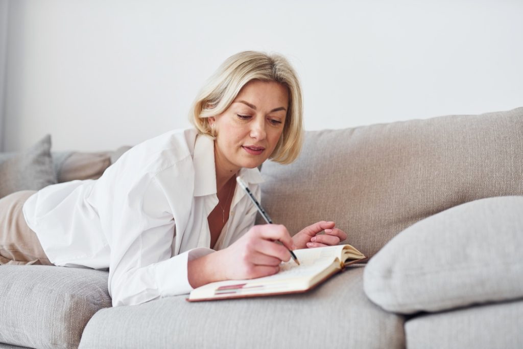 Woman in menopause writing in notebook to record progress towards wellness goals