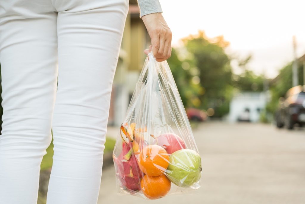 Mature woman walking with bag of raw fruits during vacation