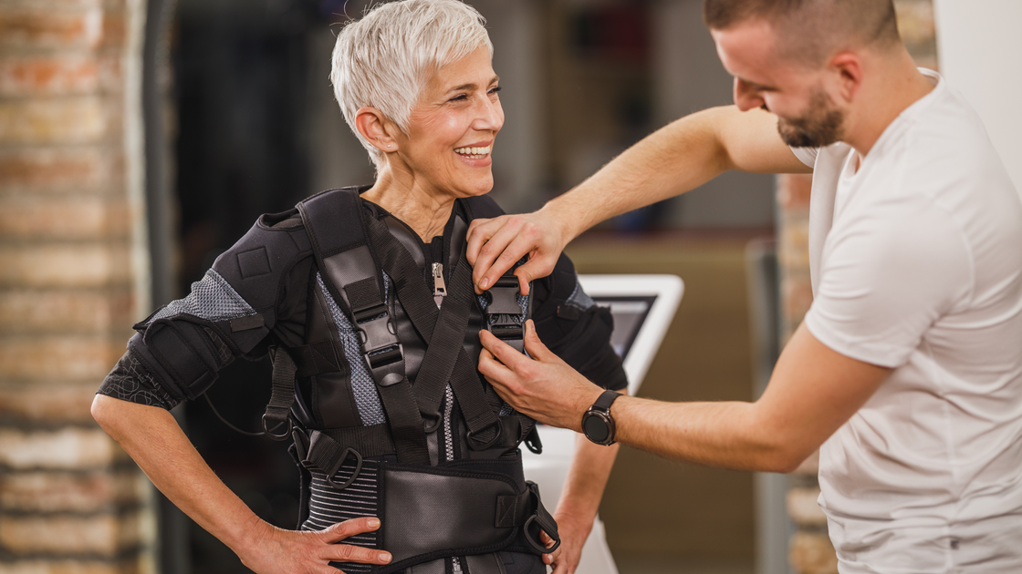 Older woman with trainer putting weighted vest on her